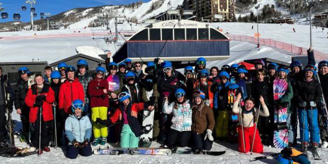 A large group of skiers are posing in front of a snowy ski mountain with a blue bird sky day behind them