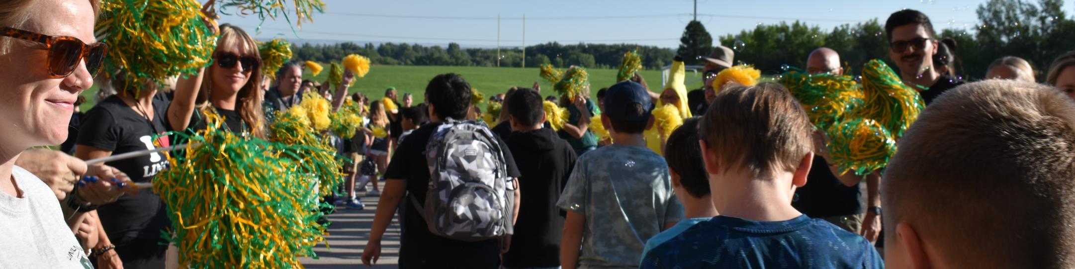 A group of teachers are waving green and yellow pompoms while students walk through the welcome tunnel on their first day of school, 2025. 