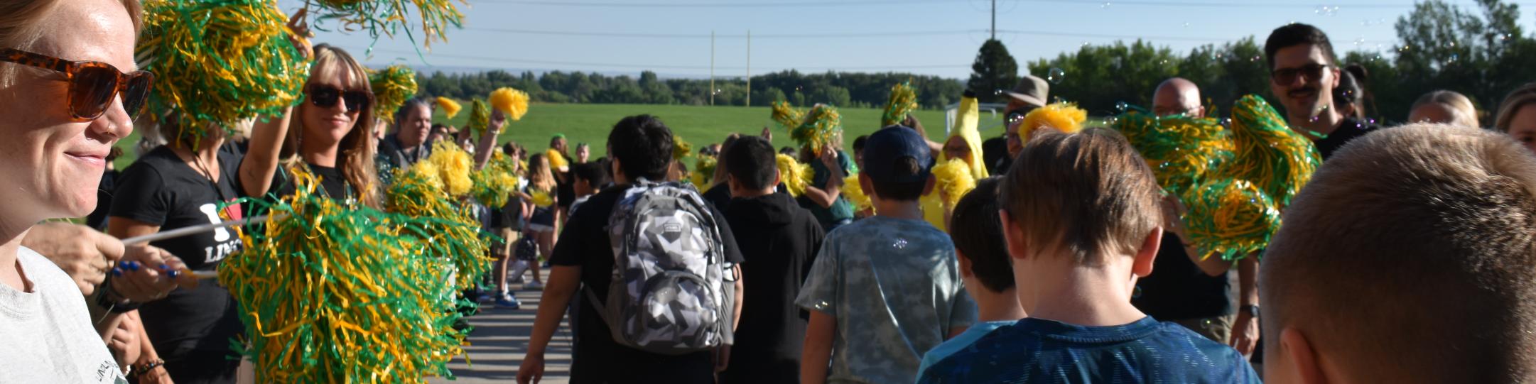 A group of teachers are waving green and yellow pompoms while students walk through the welcome tunnel on their first day of school, 2025. 