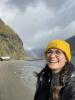 Photo of me (yellow beanie, glasses, brown hair in braids) on one of my hiking adventures. I saw a rainbow on the beach in Norway and was so overjoyed!