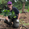 A female wearing a purple hat who is kneeling down while planting a tree.