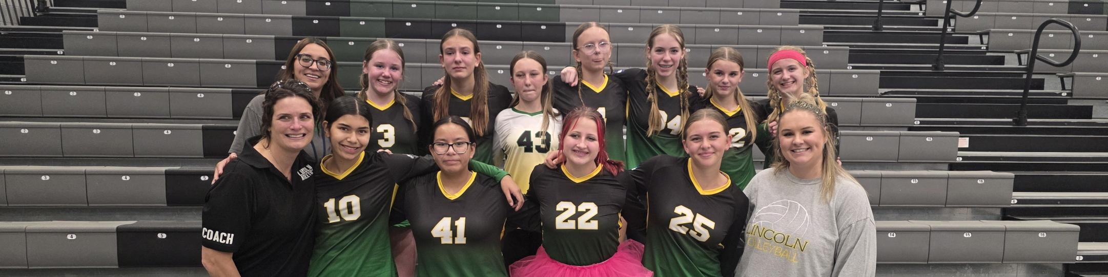 A group of girls and 2 women are smiling because they have just been crowned 3rd place champs in the Gold Bracket of the Volleyball Championships.