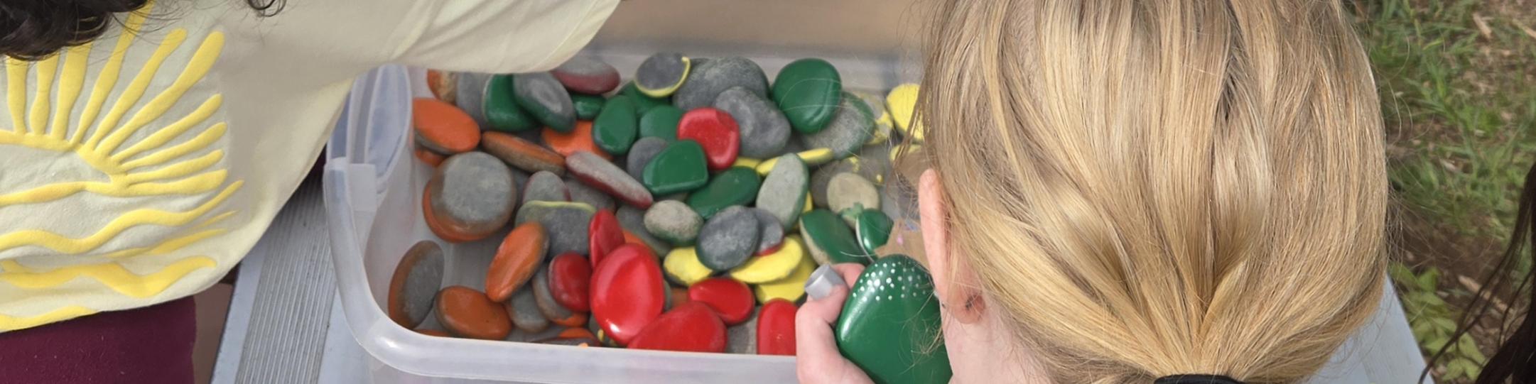 A group of middle school kids paint rocks at a park