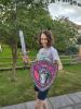 Female teacher with short, dark, curly hair weaing glasses and a Lincoln Lancers t-shirt holding a Lego shield and sword.