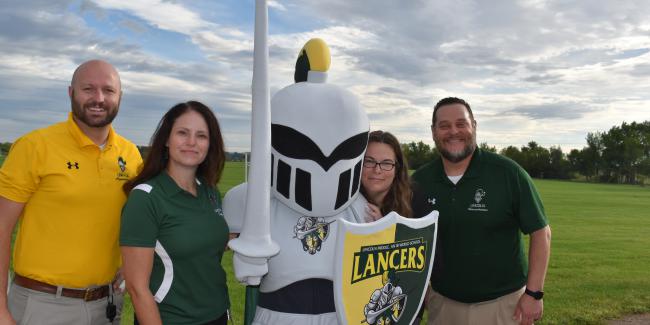 A person in a Lancer costume is posing with four adults. They are standing outside under a beautiful cloudy and blue sky