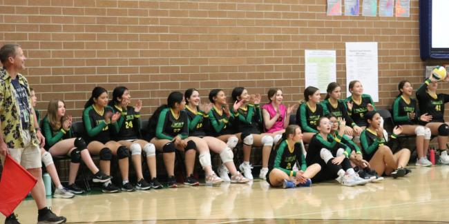 The girls volleyball team waits on the sidelines in chairs for the game to start.