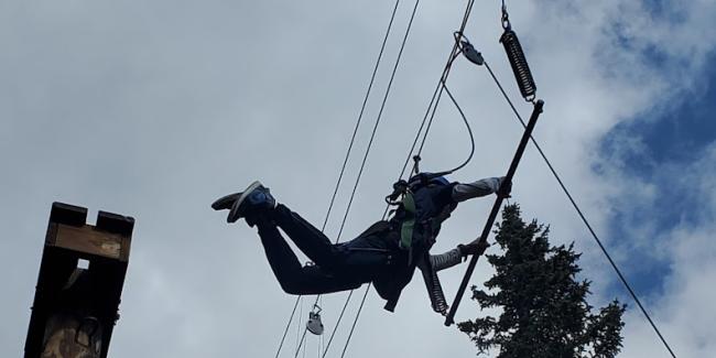 A student is on an obstacle coarse high up in the air swinging from a bar. 