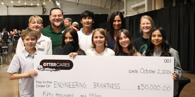 A group of students and adults are holding a large check from OtterCares in the amount of $50,000 for Engineering Brightness. Engineering Brightness is a class at Lincoln.