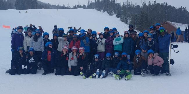 A large group of people are in ski gear posing on the mountain for a group photo