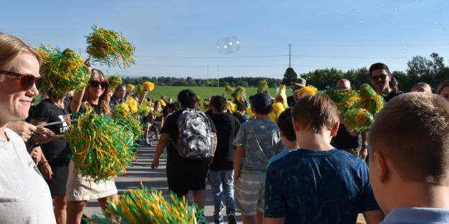 A group of teachers are waving green and yellow pompoms while students walk through the welcome tunnel on their first day of school, 2025. 