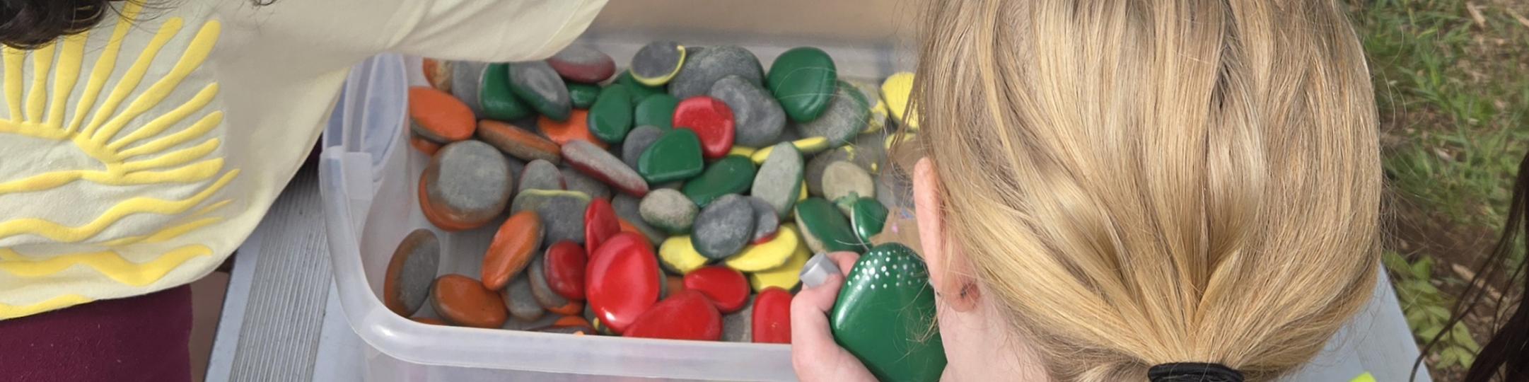 A group of middle school kids paint rocks at a park