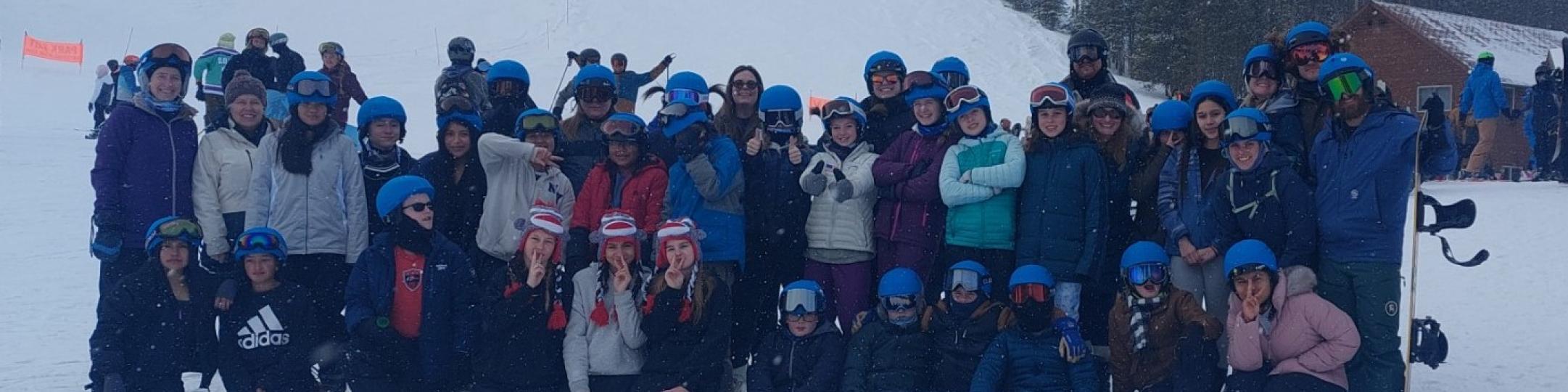 A large group of people are in ski gear posing on the mountain for a group photo