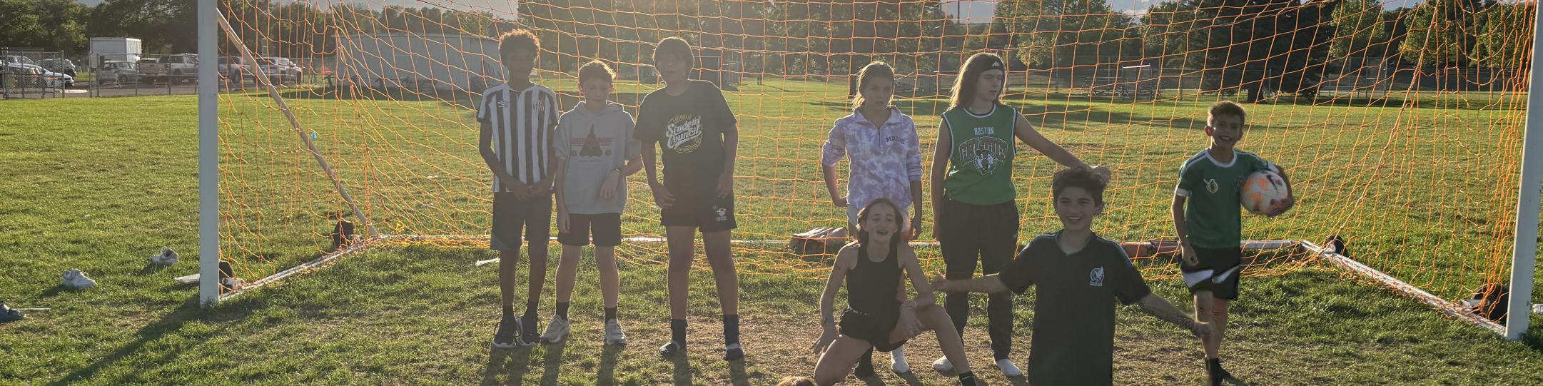 Students are posing in front of a soccer net. The sun is setting behind them. T