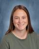 A school photo of a female teacher with brown hair, on a blue background, wearing a green shirt, smiling.