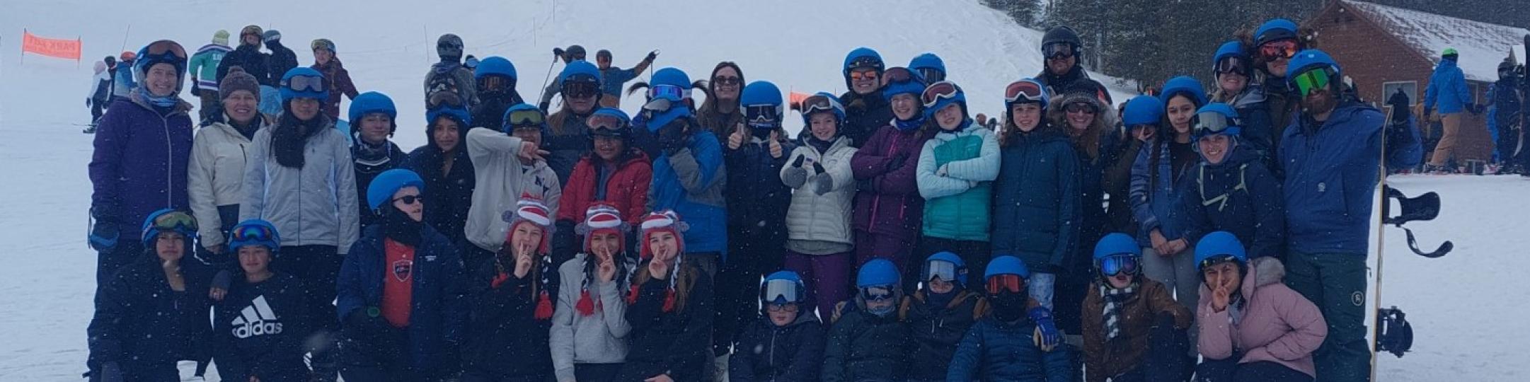 A large group of people are in ski gear posing on the mountain for a group photo