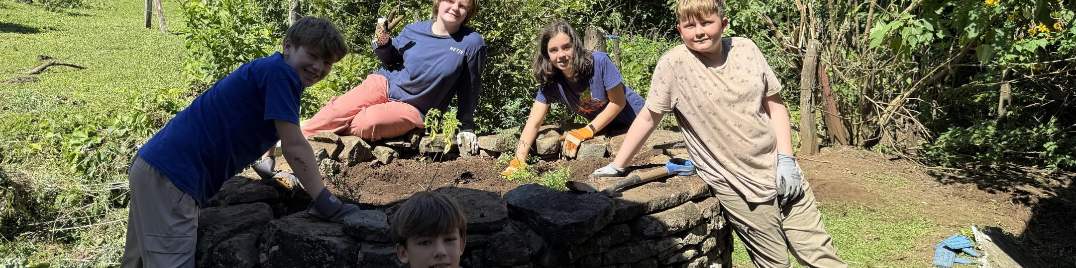 5 students are wearing gloves and planting plants during a Service Learning trip to Costa Rica.